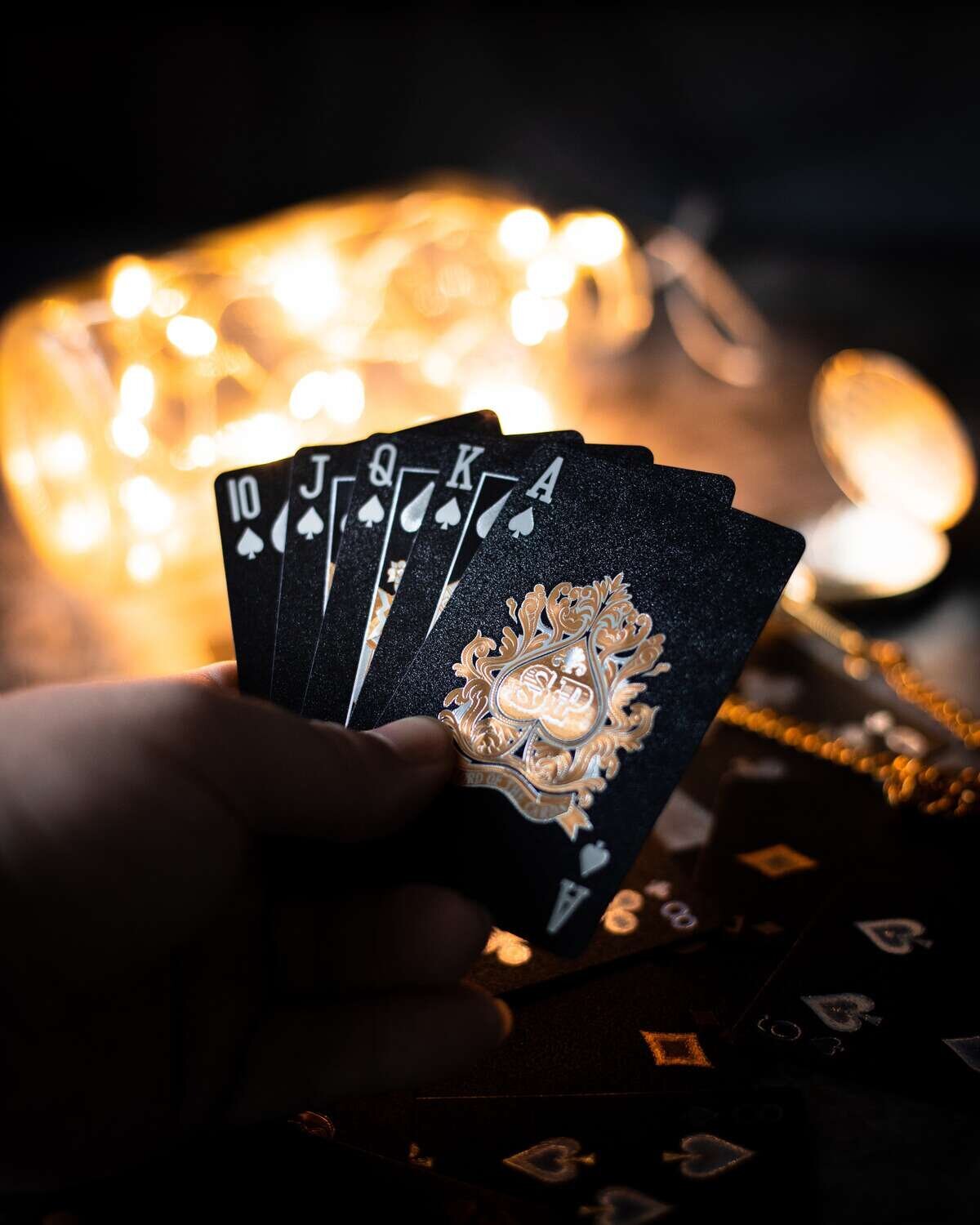 Hand holding black and gold playing cards displaying the ace of spades