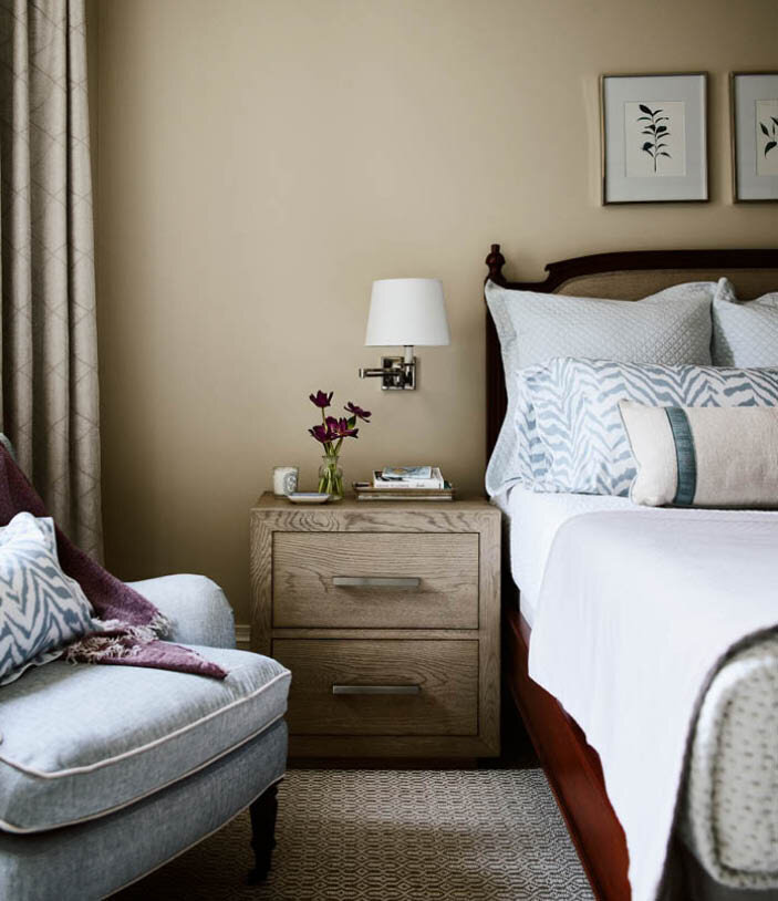 A classic walnut bed paired with a cerused oak bedside table, soft blue chair, neutral linen drapes, and floral art create a timeless bedroom. By Sarah Scales.