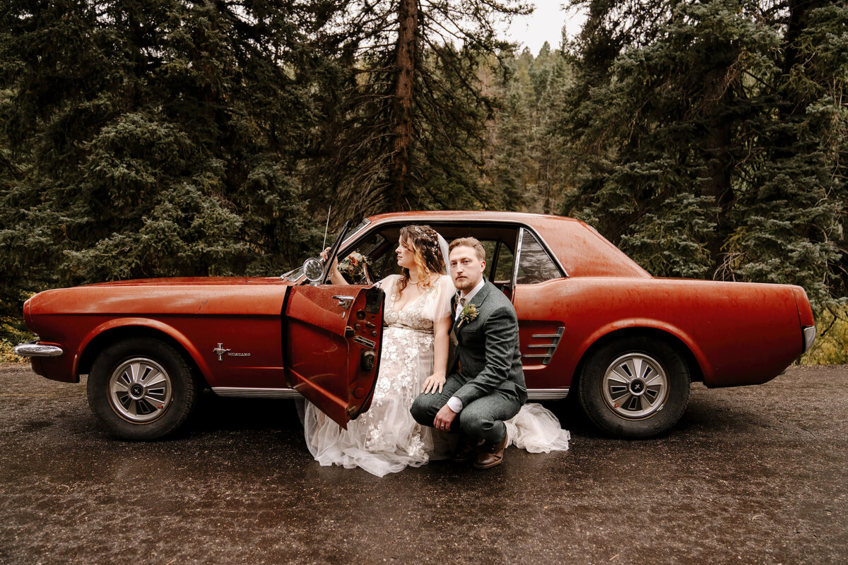 bride and groom by red car