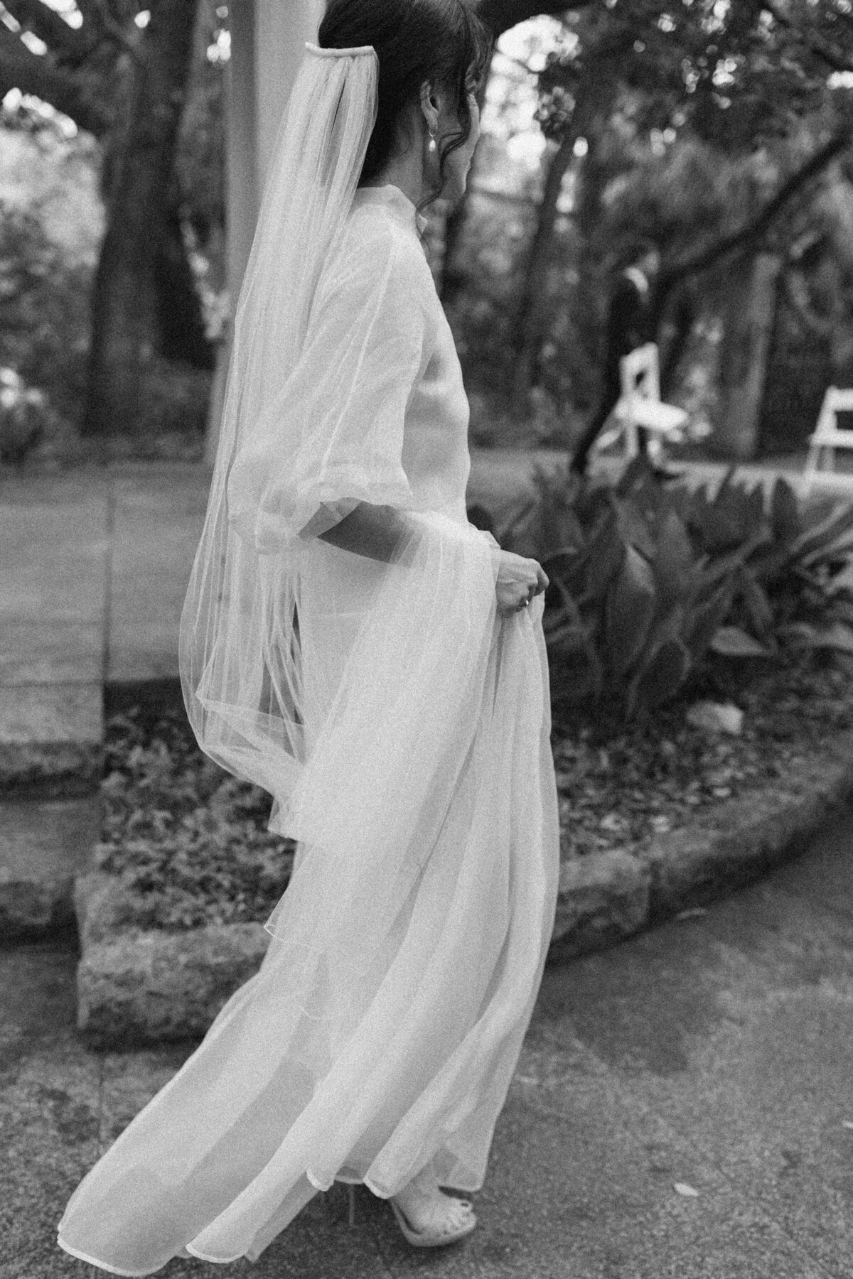 Bride holding her veil and walking  in the grounds of Laguna Gloria in Austin