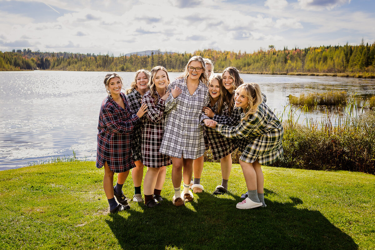 Bridal party in flannel pajama gowns laughing and huddling around bride in NH wedding getting ready photos