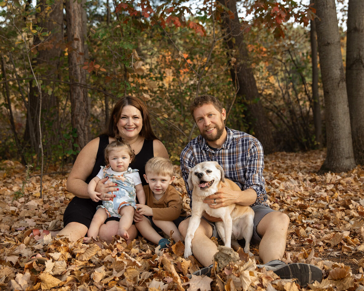 Mom, Dad, little boy and baby girl sitting in leaves with their senior dog on a beautiful fall evening.