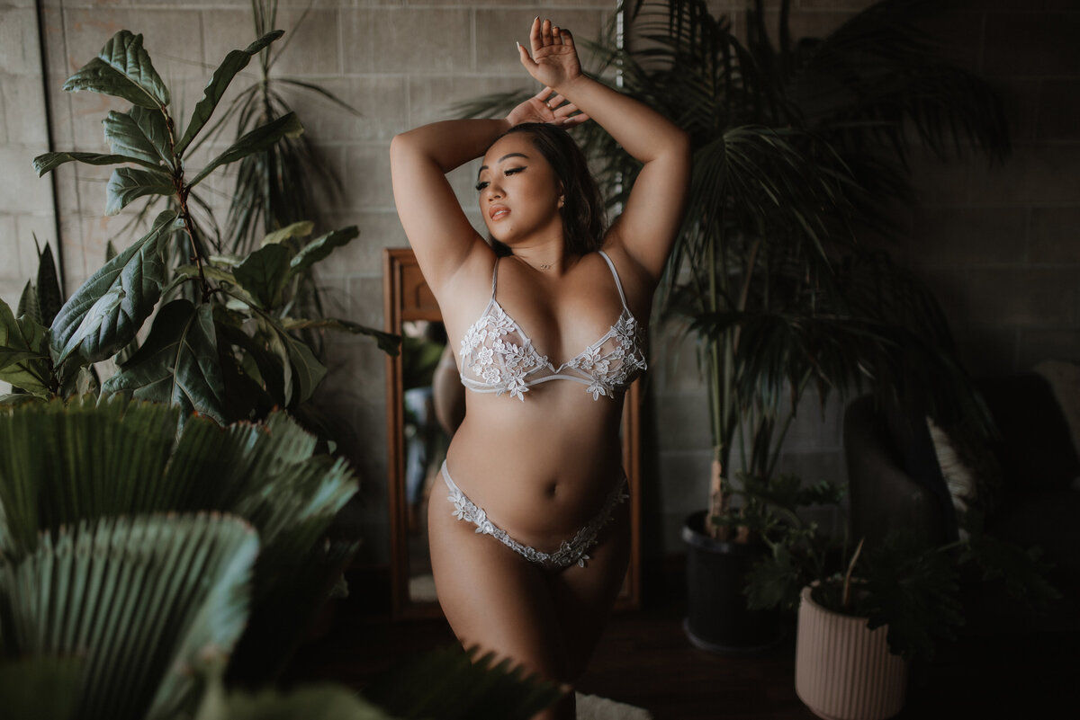 A woman in white lingerie poses with her arms overhead surrounded by plants in the Vancouver, BC boudoir studio.