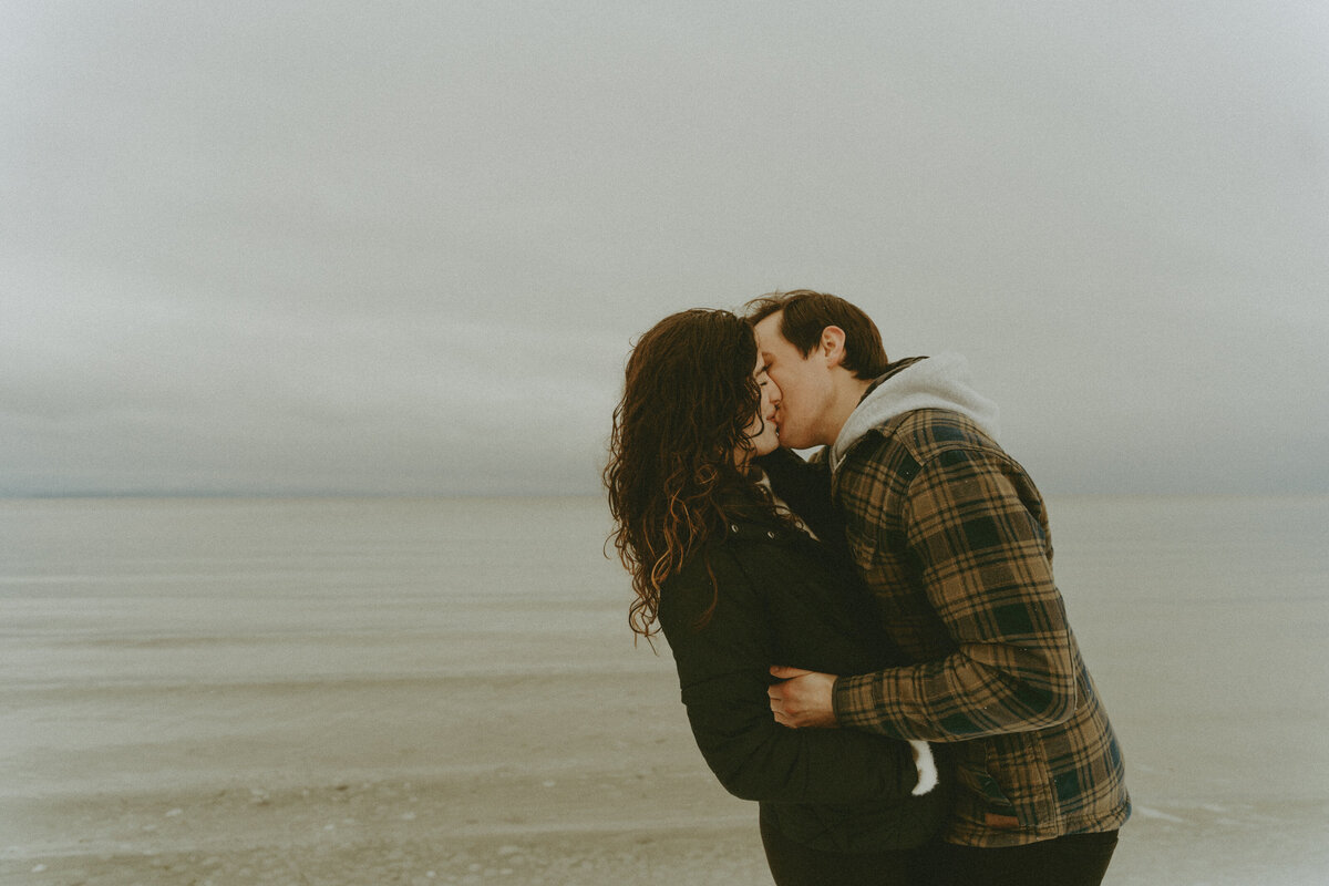 wintry engagement photo of a boy kissing a girl cuddled up