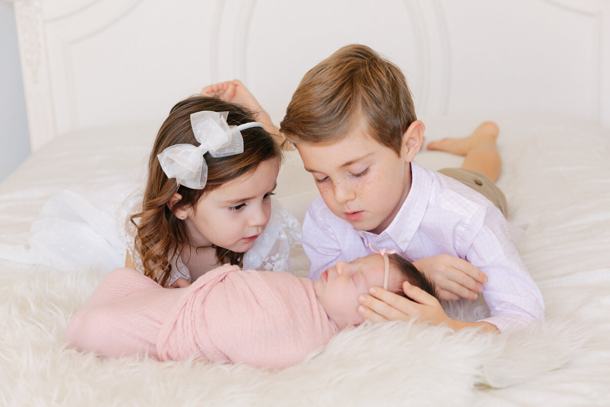 Two small kids laying on a bed with their newborn sibling