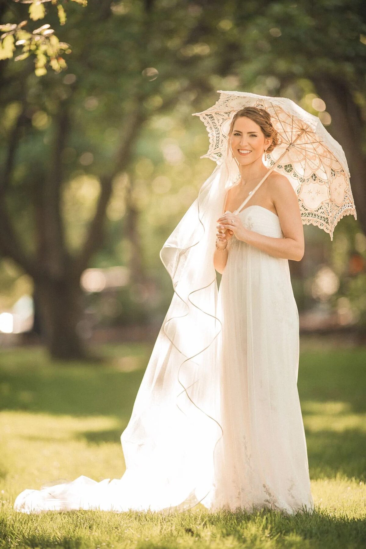 A bride under the shade of a lace parasol shines with happiness, the soft sunlight highlighting her bridal glow.