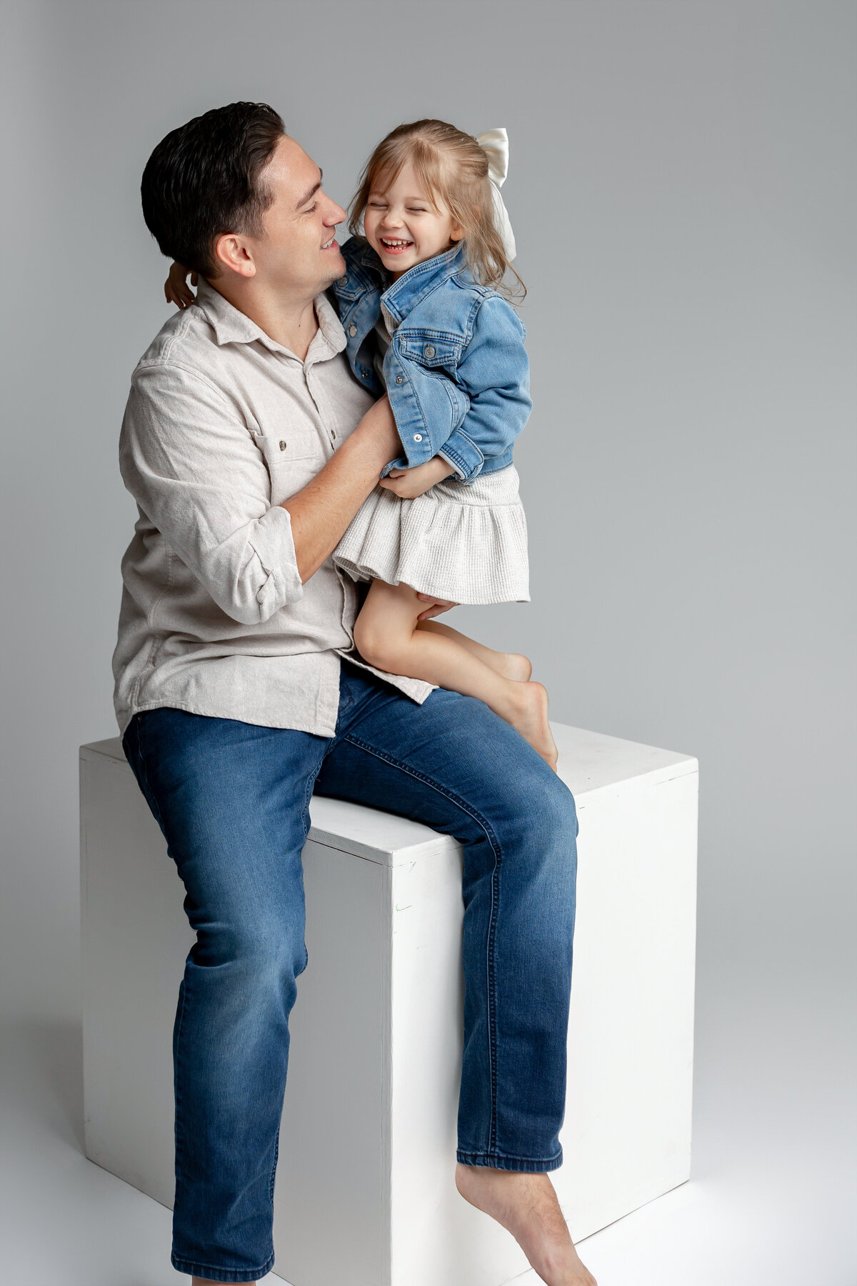 Father holding young daughter while mother looks on, captured in simple studio style. Photographed by Yucaipa family photographer Kaitlyn Dawn Photography.