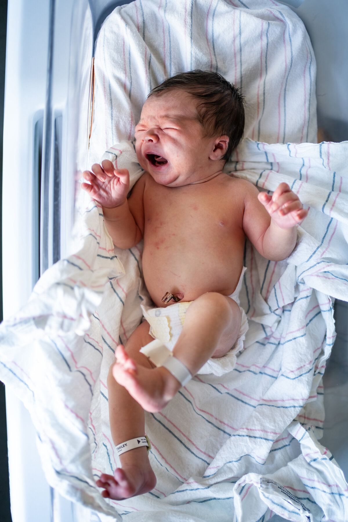 Crying newborn in bassinet on hospital blankets