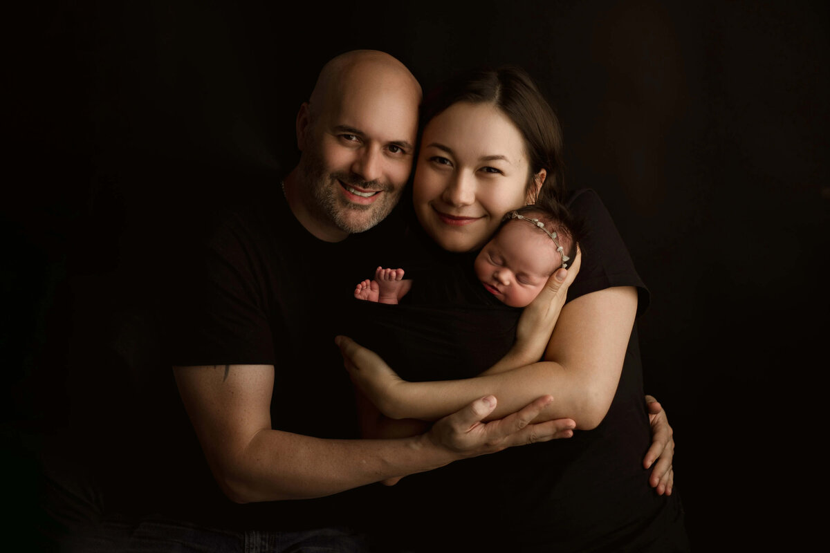 Family snuggled with newborn on dark backdrop - timeless newborn session near Minneapolis