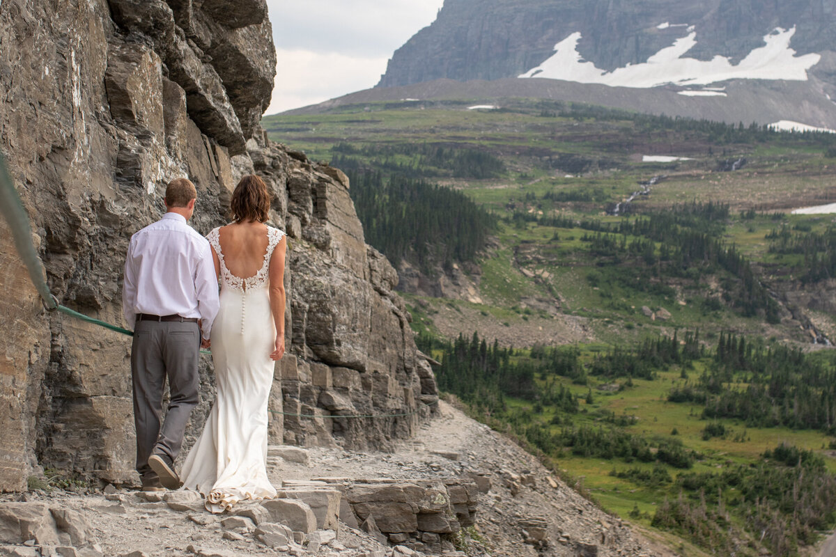 A bride and groom walk along a narrow trail on their elopement day in Glacier National Park Montana.
