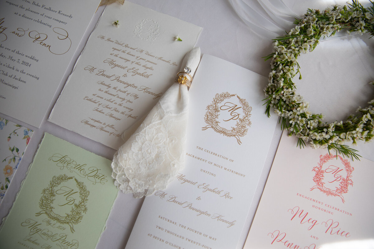 A flat lay of wedding invitations, bride's handkerchief, wedding program, and engagement ring.