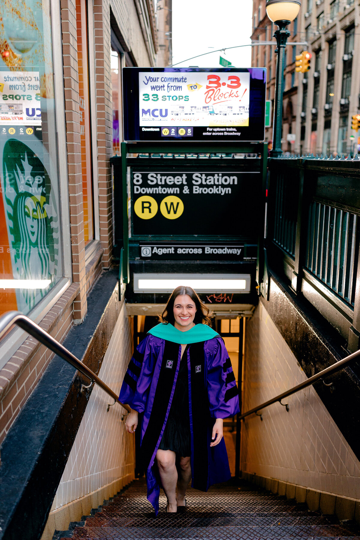 NYU graduate walking up the stairs at a subway station in NoHo while wearing purple gown.