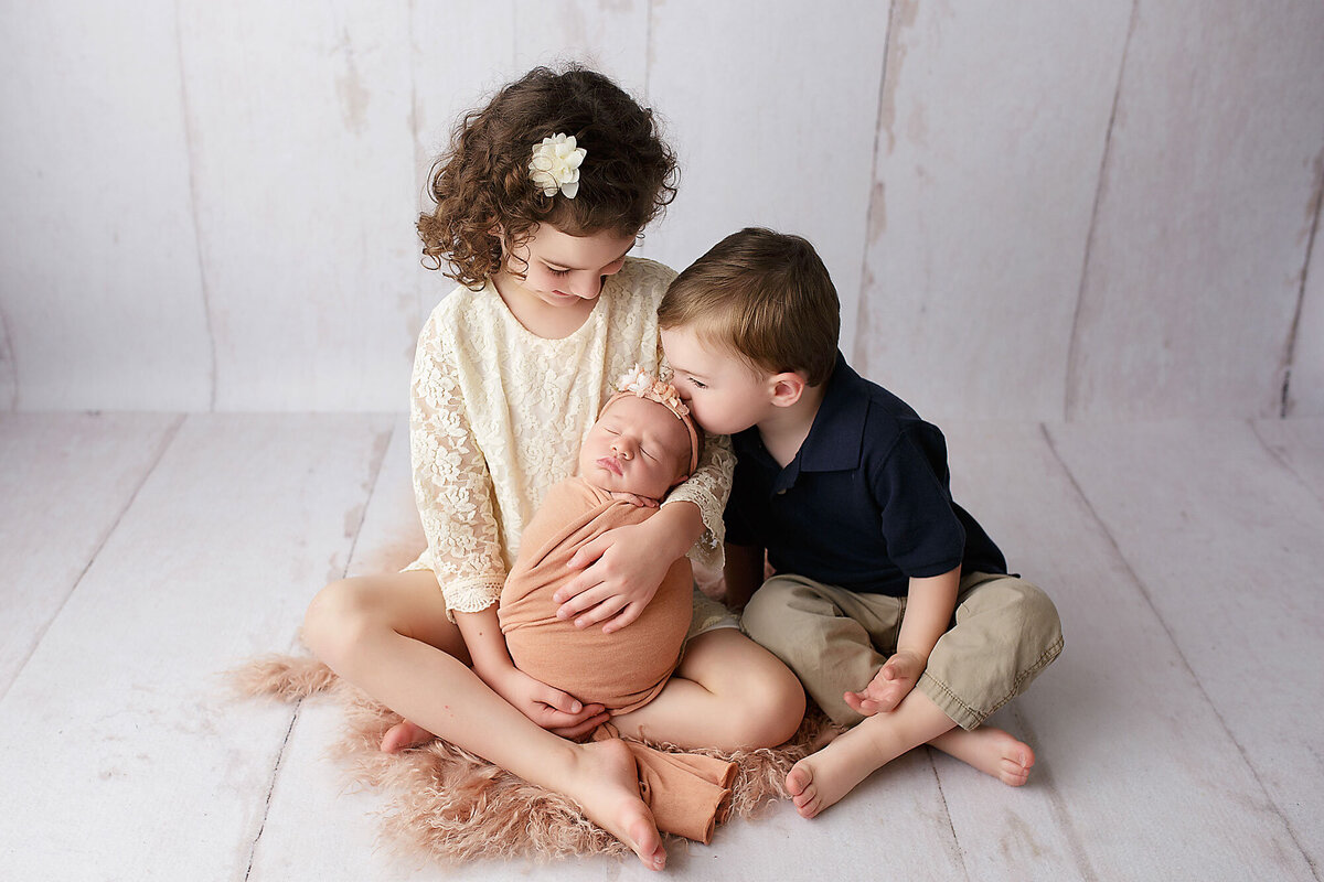 siblings holding and kissing newborn baby girl