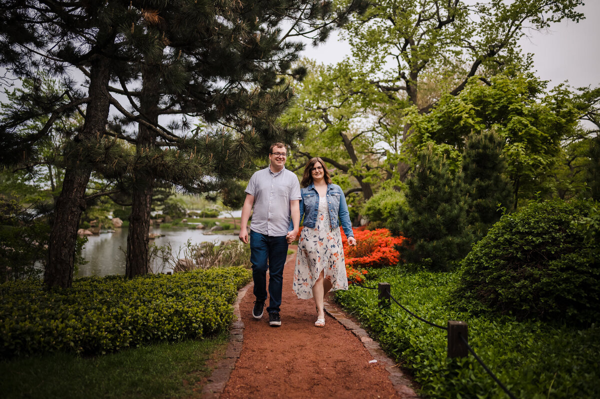 A couple holds hands while walking down a path in Japanese Garden
