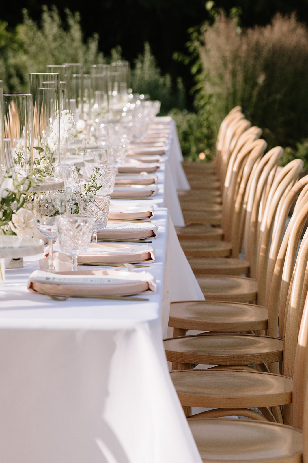 Long banquet table with neutral linens, florals, and candles — elegant outdoor dinner setup for an intentional, guest-centered celebration.