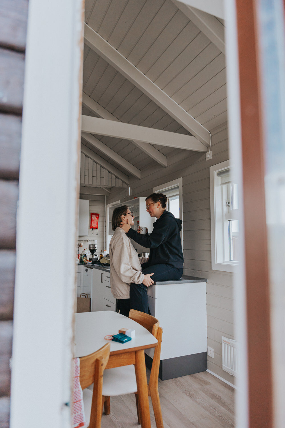 Woman sits on the countertop while smiling at her wife 