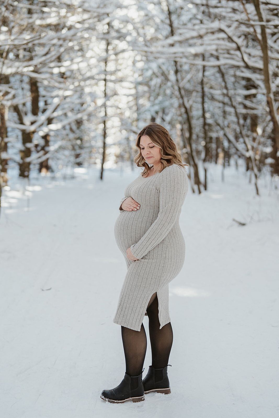 Pregnant woman standing in the snowy woods at Al Sabo Preserve in Kalamazoo Michigan during her winter maternity photo session.