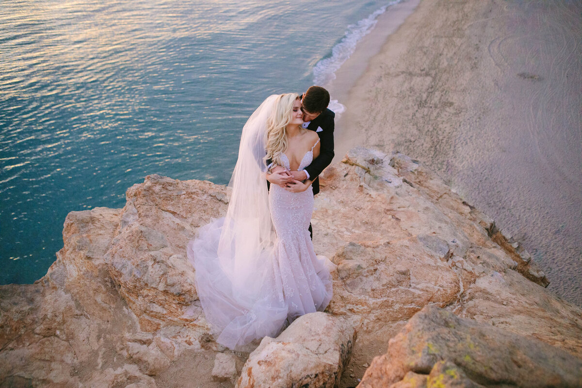 bride and groom kiss over ocean