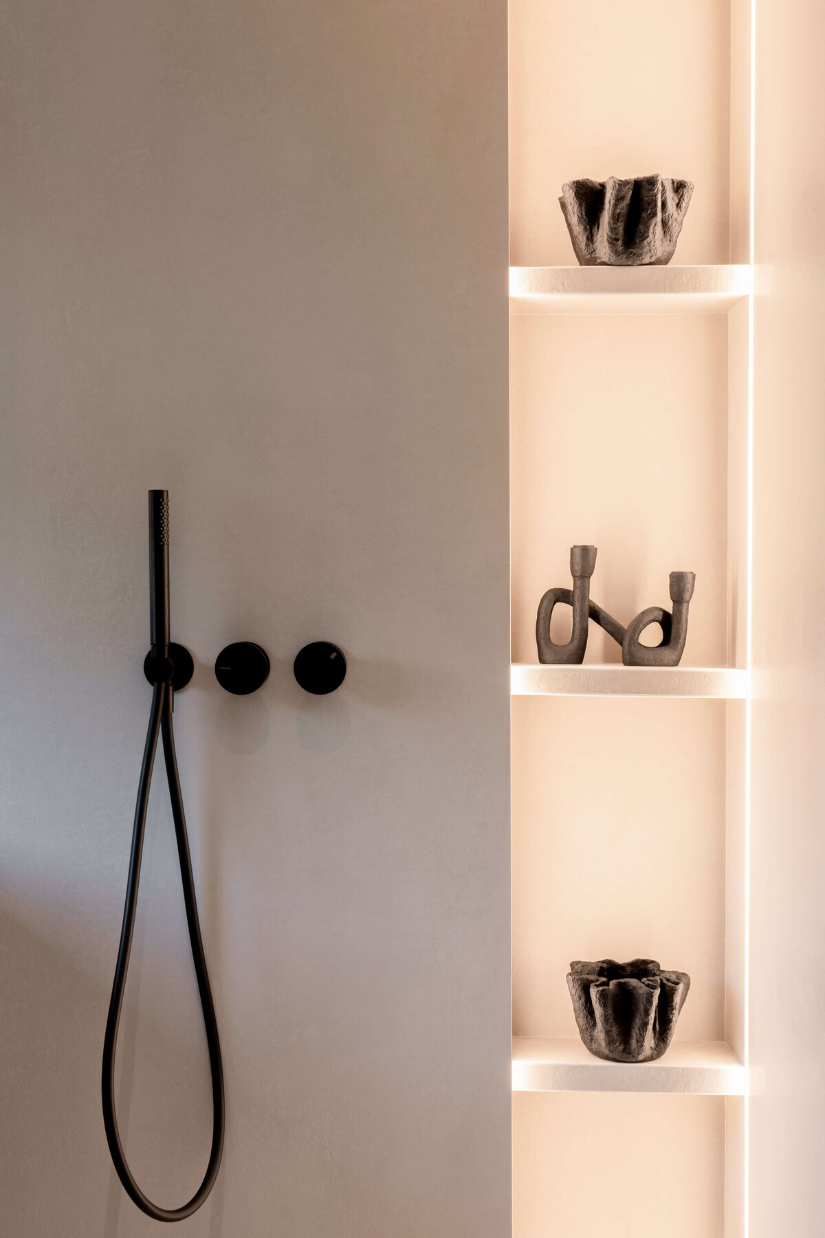 Sleek neutral walk-in shower that has built-in shelves emitting a soft, warm light. The shower hardware is start black, adding a dramatic edge to the shower.