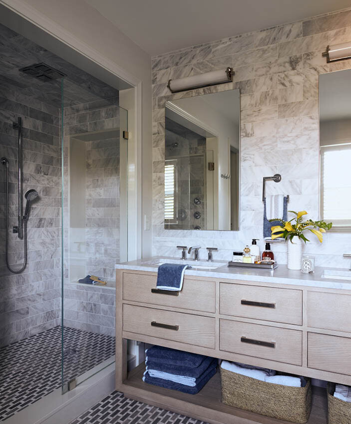 Explore the luxurious primary bathroom in a historic Hingham home, featuring an oak vanity, mosaic tile flooring, and a walk-in shower with Carrara marble wall tiles.