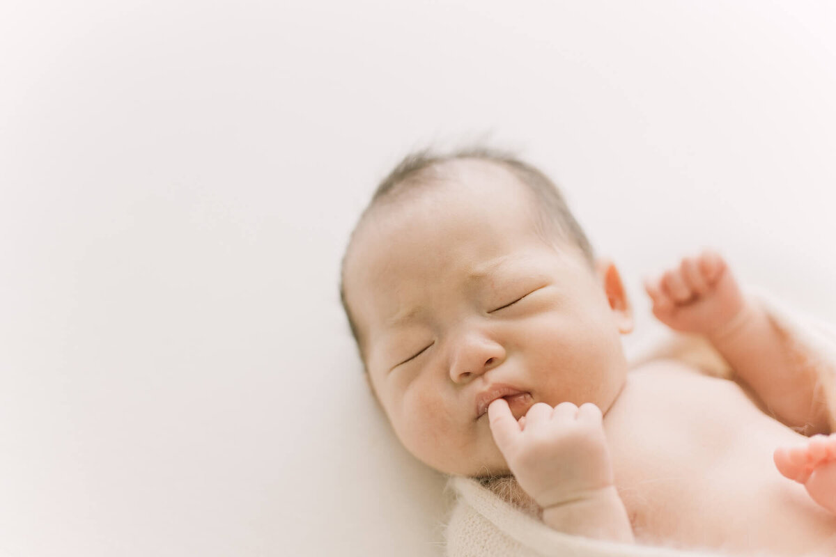 口に指を入れて眉間にしわを寄せている姿が何とも可愛らしい新生児の赤ちゃんのニューボーンフォト