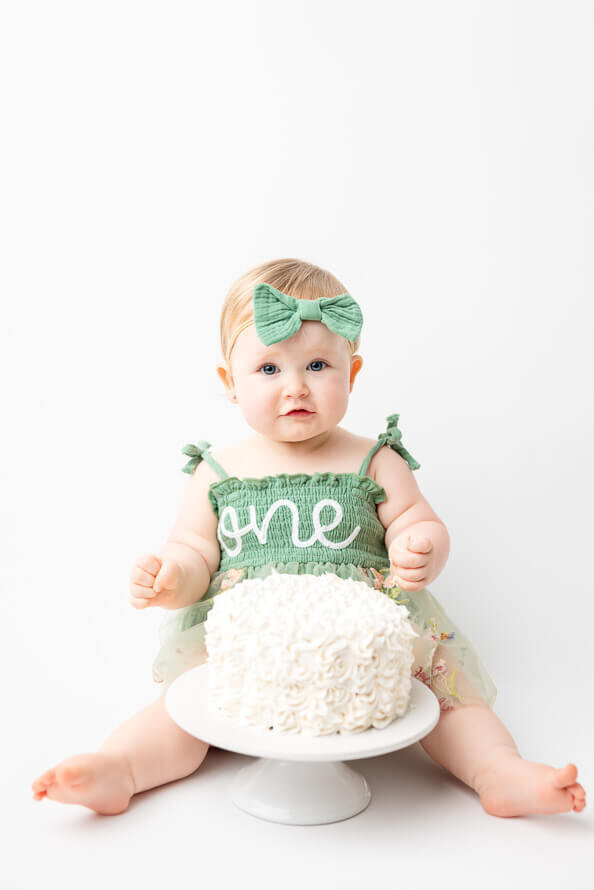 Baby poses with her cake during her cake smash session in the studio.