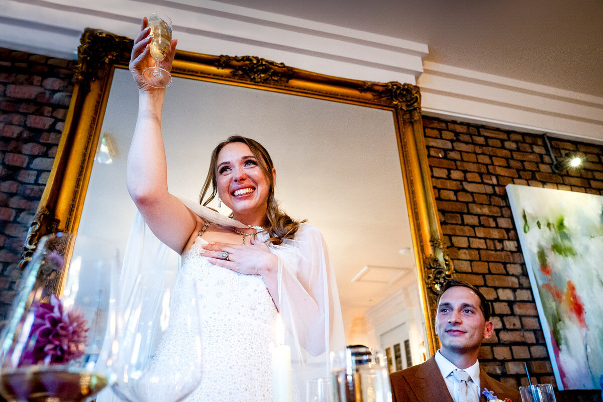 A bride crying and holding her hand to her heart as she raises a champagne flute to her guests at a wedding in the square club bristol