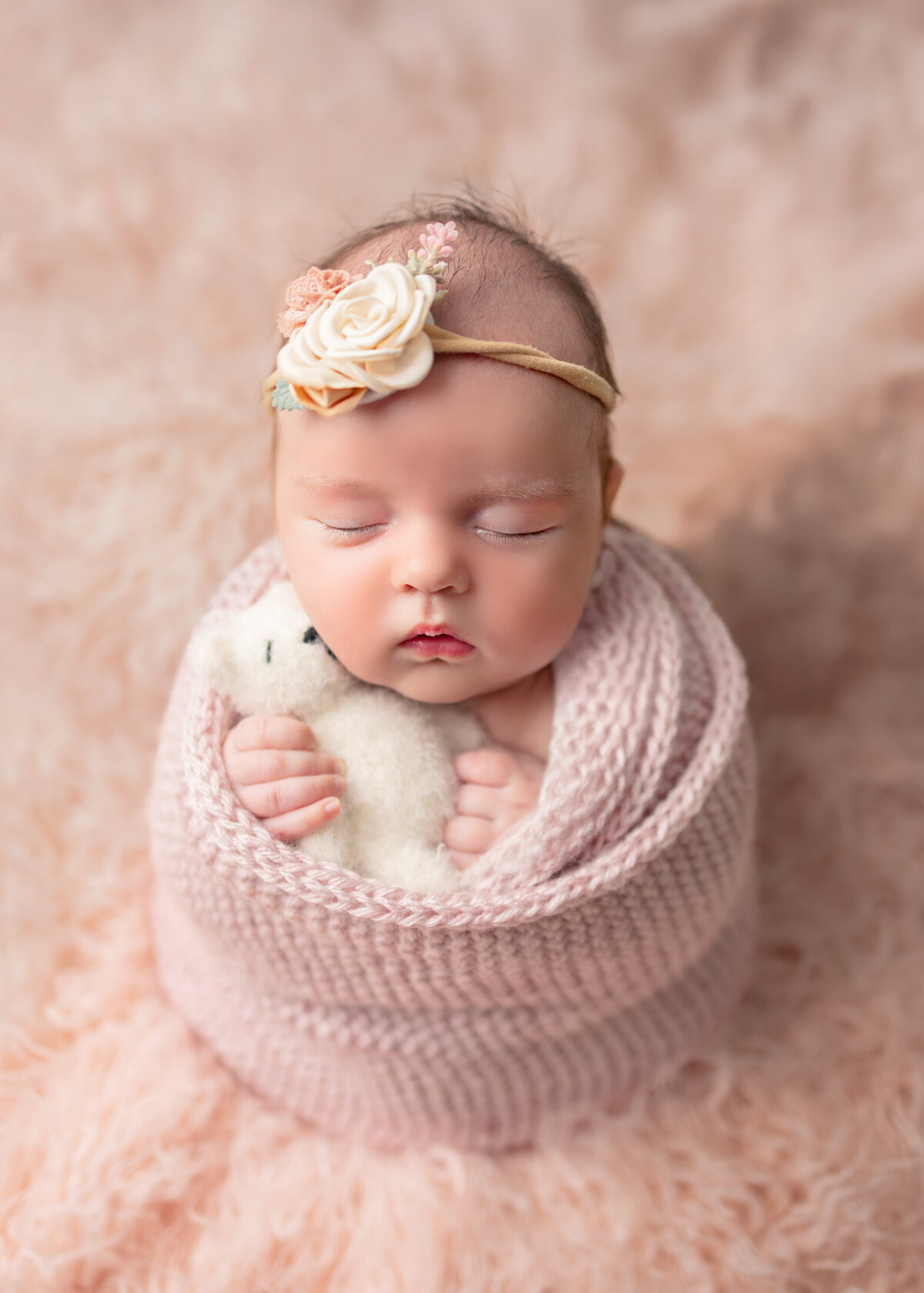 Newborn baby girl wrapped in soft pink knit blanket holding a tiny white teddy bear during studio newborn session in NJ