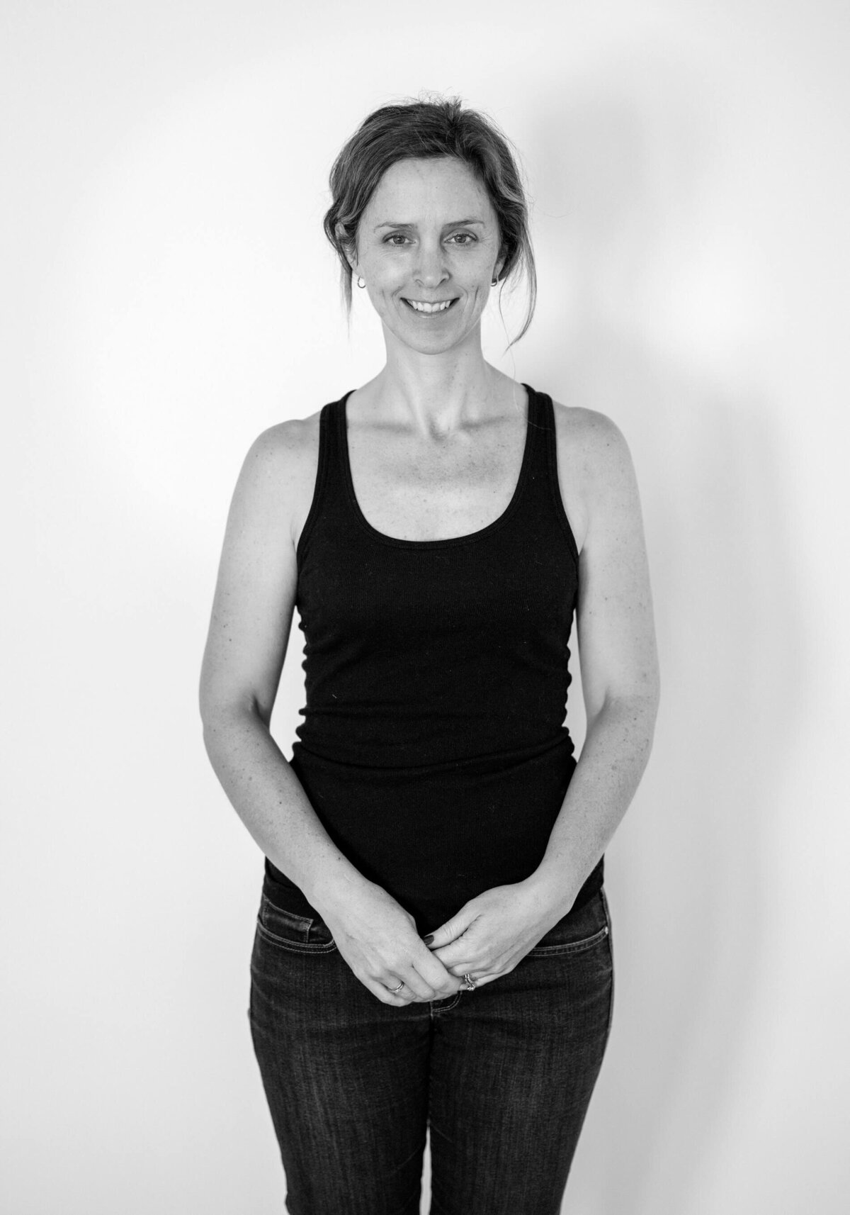 Studio before shot of a woman in a black tank top, smiling with her hair in a bun.