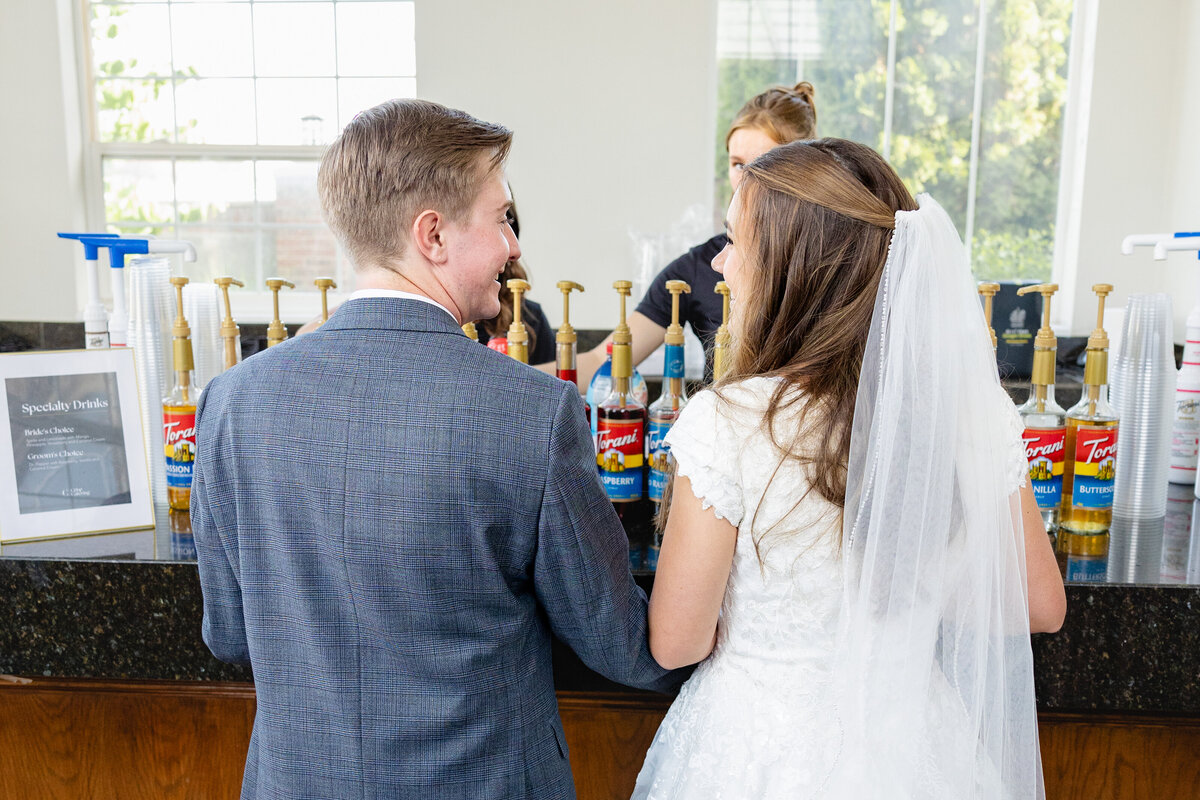 A bride and groom stand at the wedding reception's specialty drink bar, choosing their custom beverages.