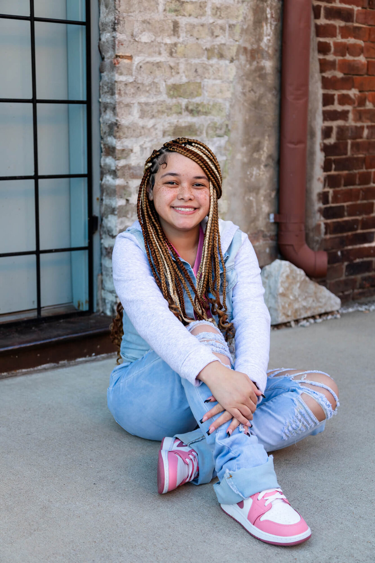 A beautiful girl sitting on a city side street wearing denim and pink and white Nike's. Captured by Springfield, MO senior photographer Dynae Levingston.