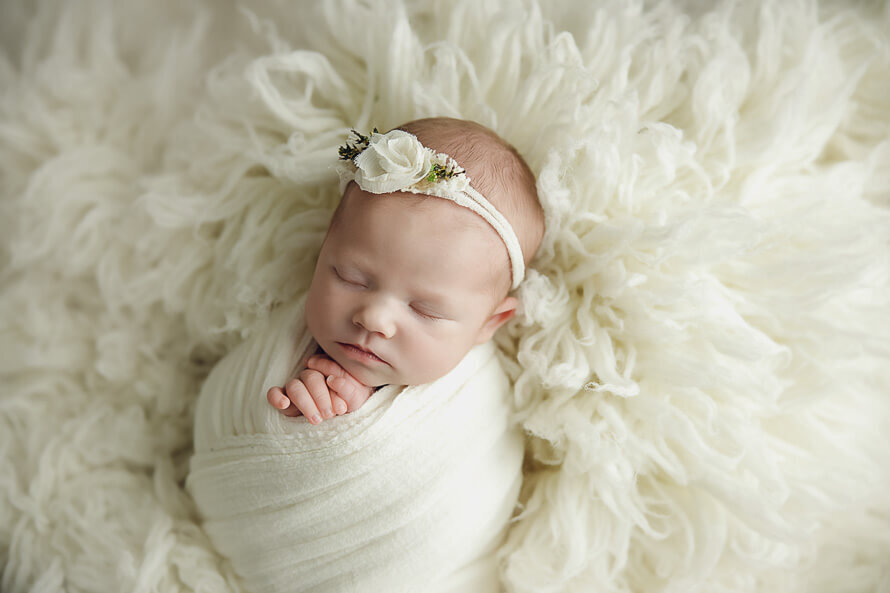 Newborn baby girl wrapped with her hands out.