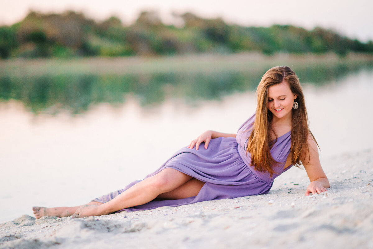 Teen girl lying in the sand at Sullivan’s Island beach wearing a purple dress during her senior session
