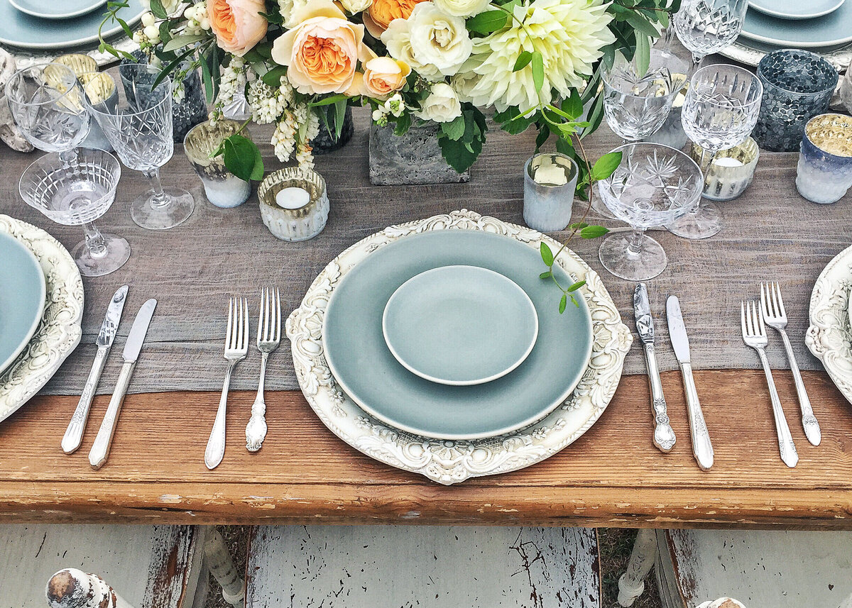 A table set for a rustic party with stoneware plates with a green and peach floral centerpiece.