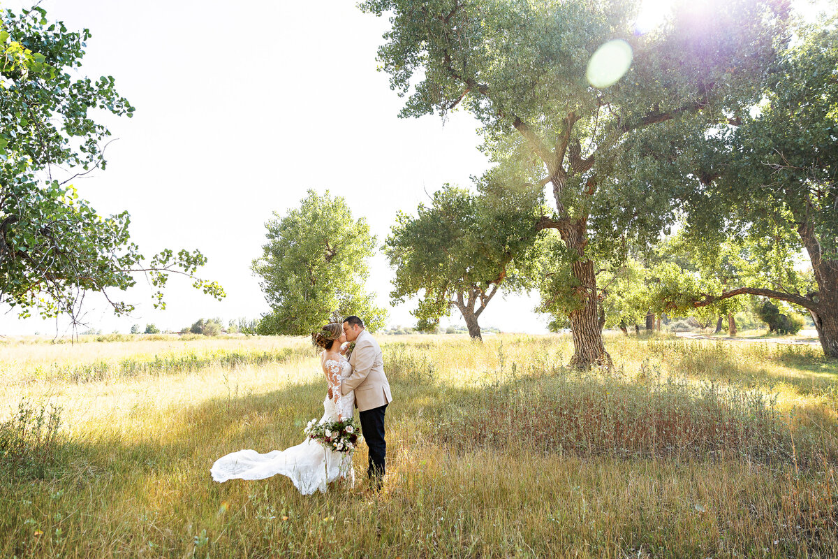 bride & groom kiss in a sunny tree lined meadow