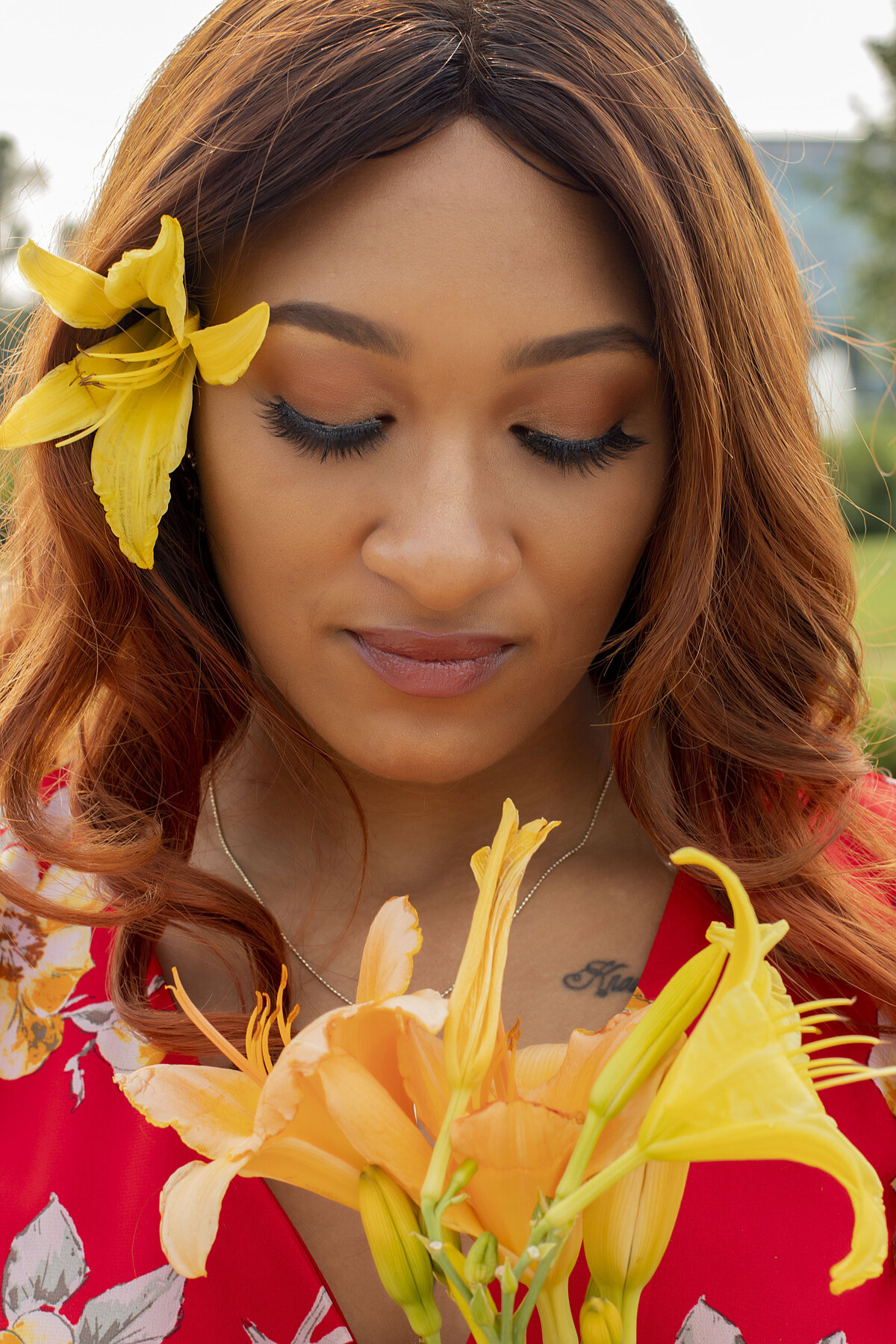 Woman in red floral dress with yellow flower in her again looking down at flowers in hand