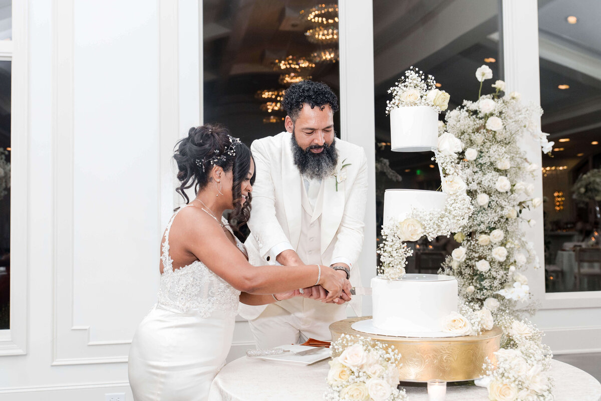 The bride and groom joyfully cut into their beautifully designed wedding cake.