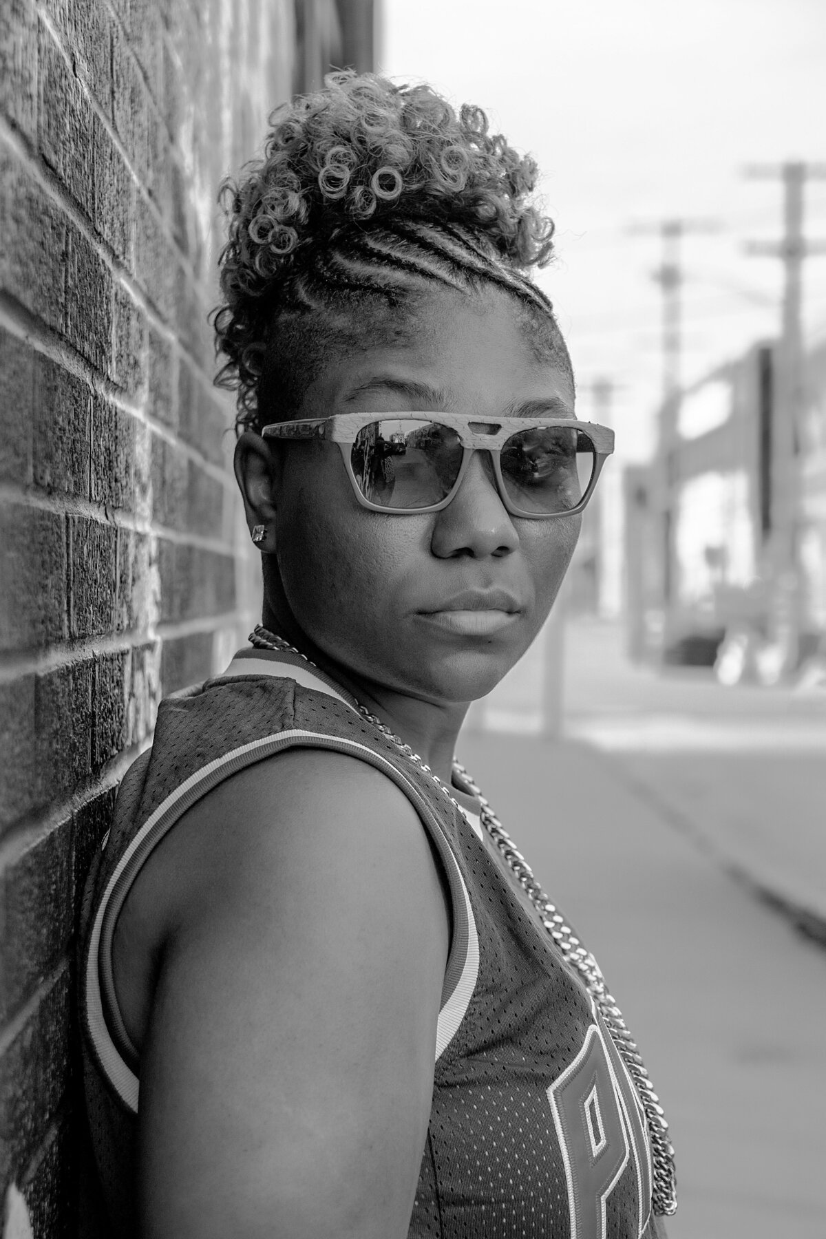 Woman in sunglasses and Detroit Pistons jersey back against a brick wall