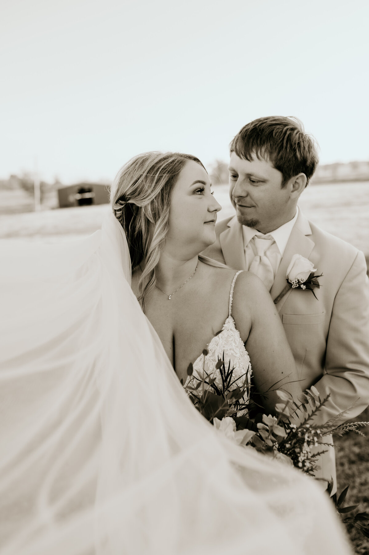 groom stands behind the bride and looks down at her and smiles as the bride looks back at him