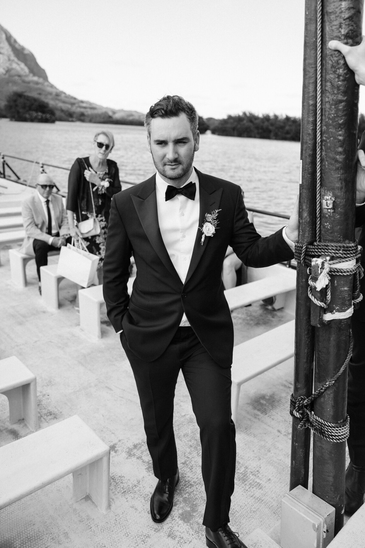 Man in a tuxedo squinting from the sun standing on a boat at kualoa ranch in black and white
