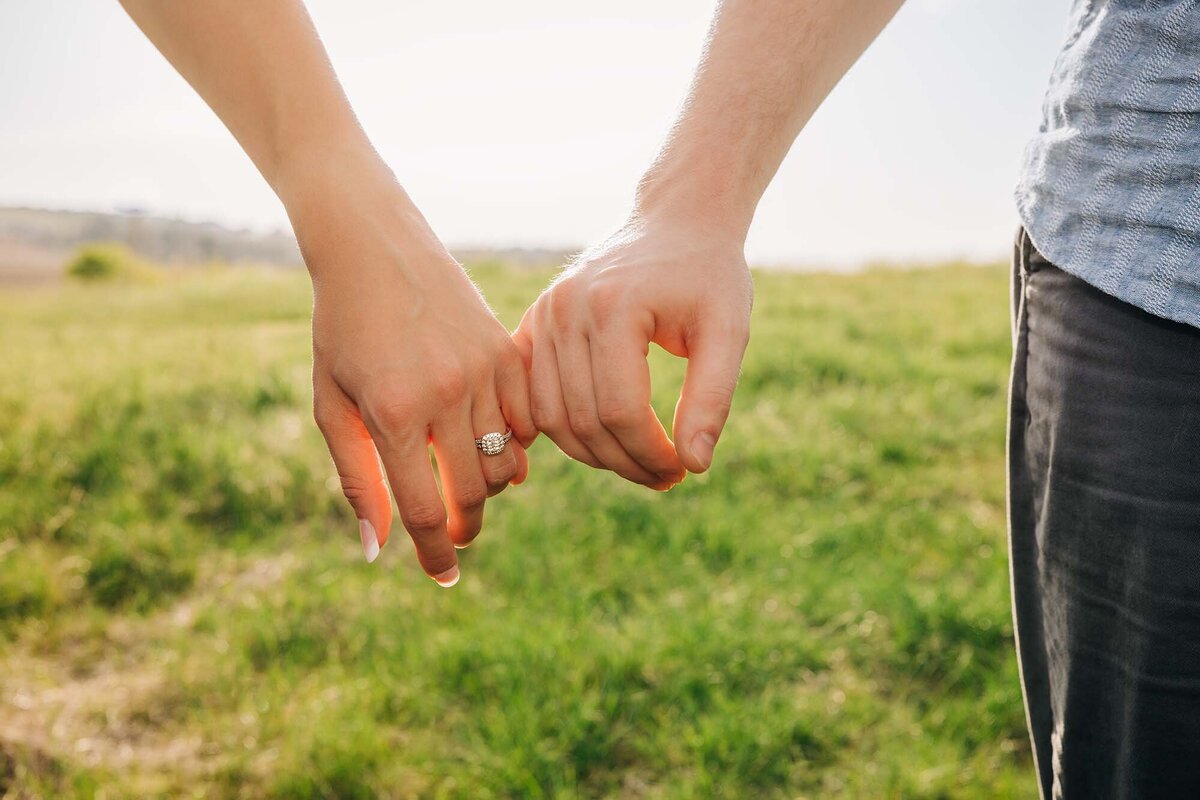 Close up photo of couple holding hands with engagement rings