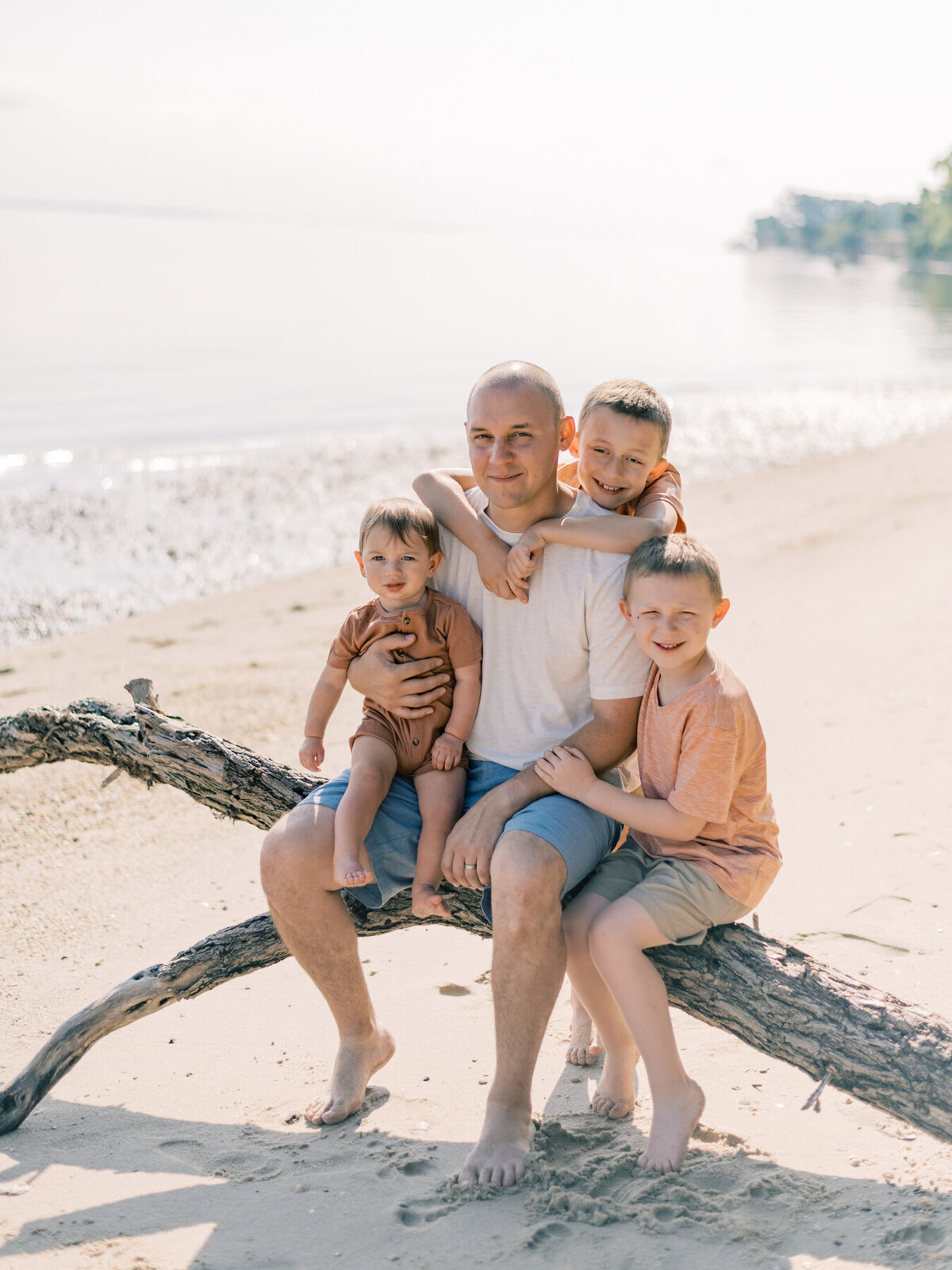 Dad with his three boys sitting on driftwood.