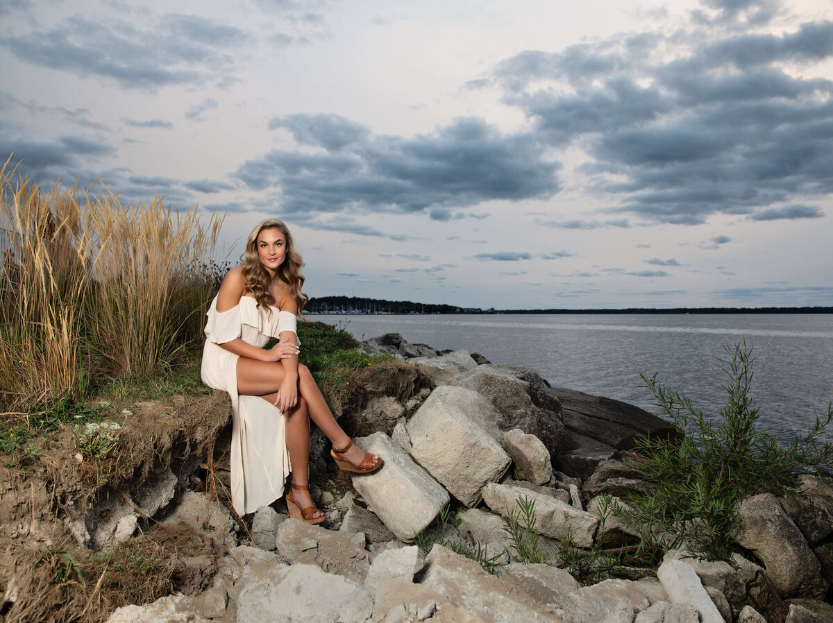 Senior portrait of a girl in a white dress sitting on grassy edge on the Erie Pa bayfront
