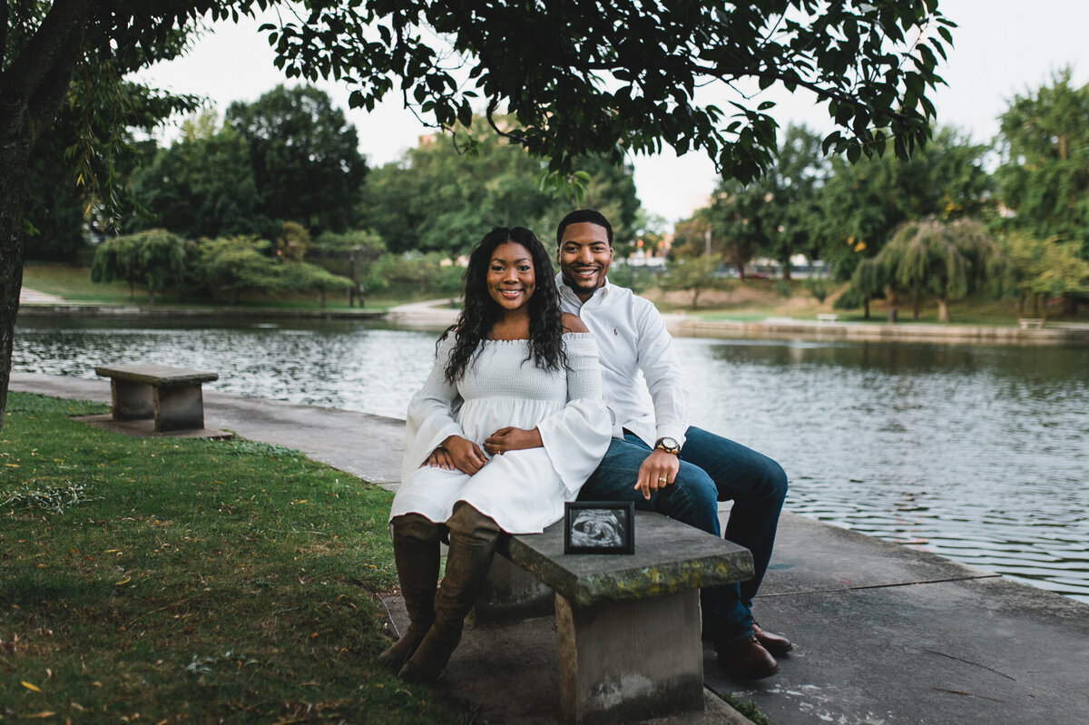 Pregnancy announcement photo with woman and man sittings on a bench outside.