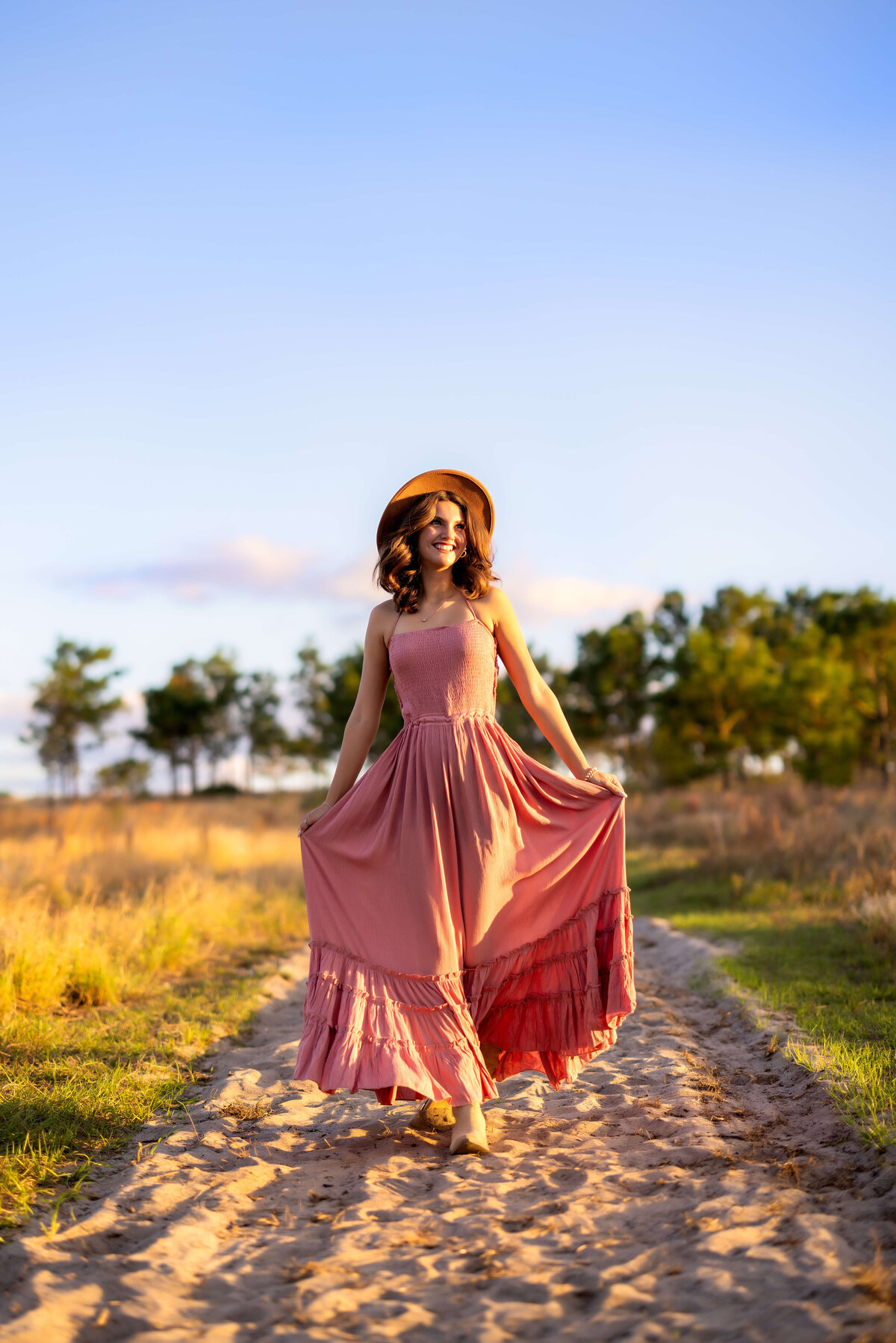 High school senior session with pink dress walking along sandy path with dress blowing in the breezy wind in Orlando