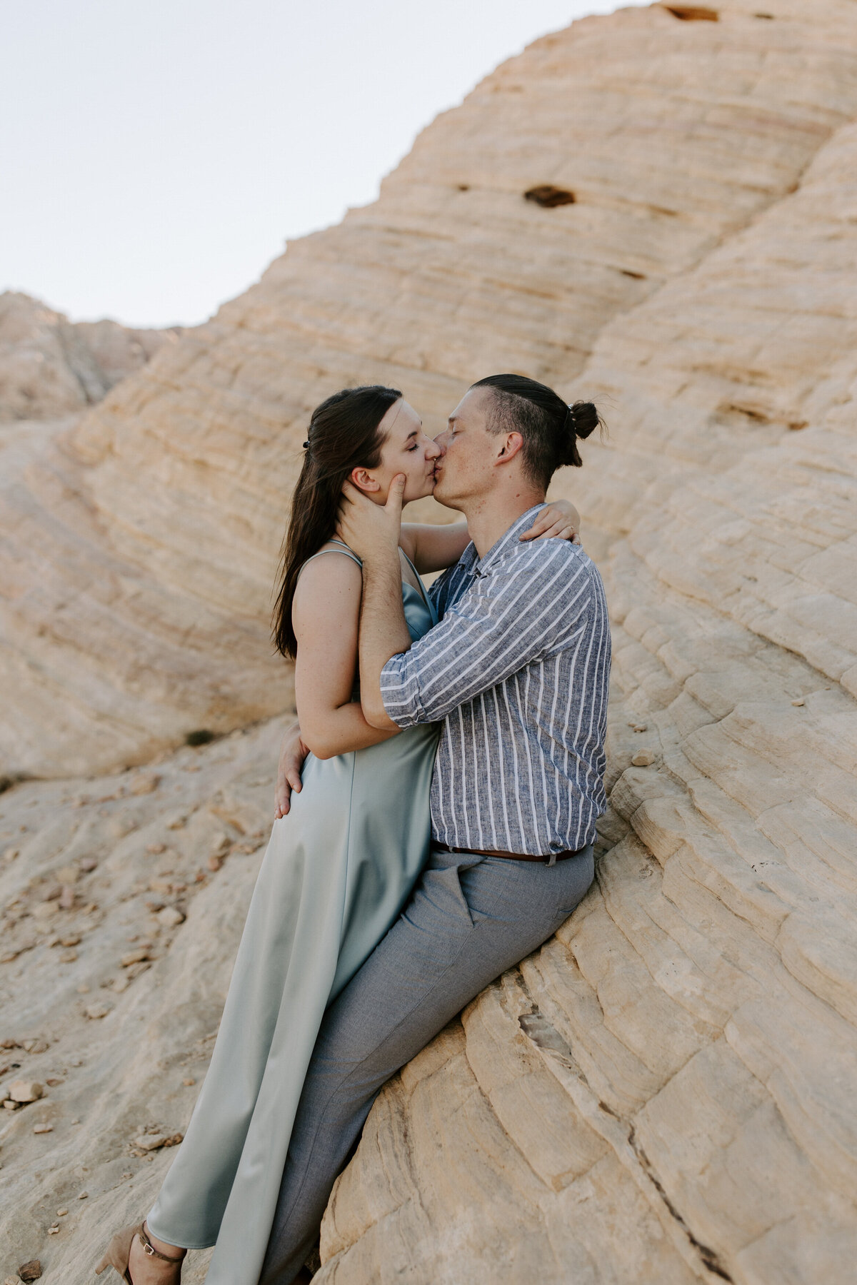 A couple kisses while leaning back on a rock.