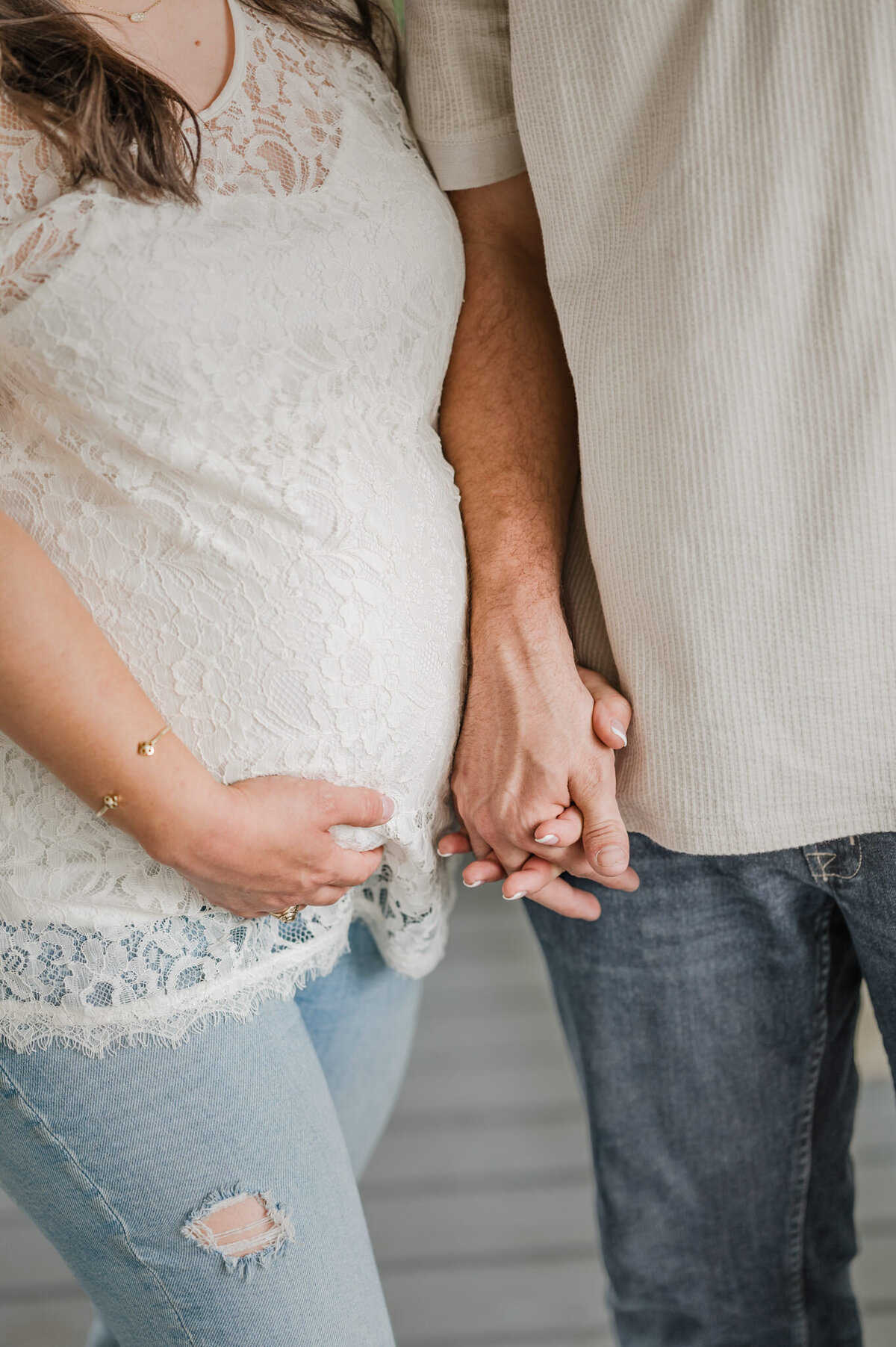 Close up picture of a man and woman holding hands and she's cradling her pregnant belly.