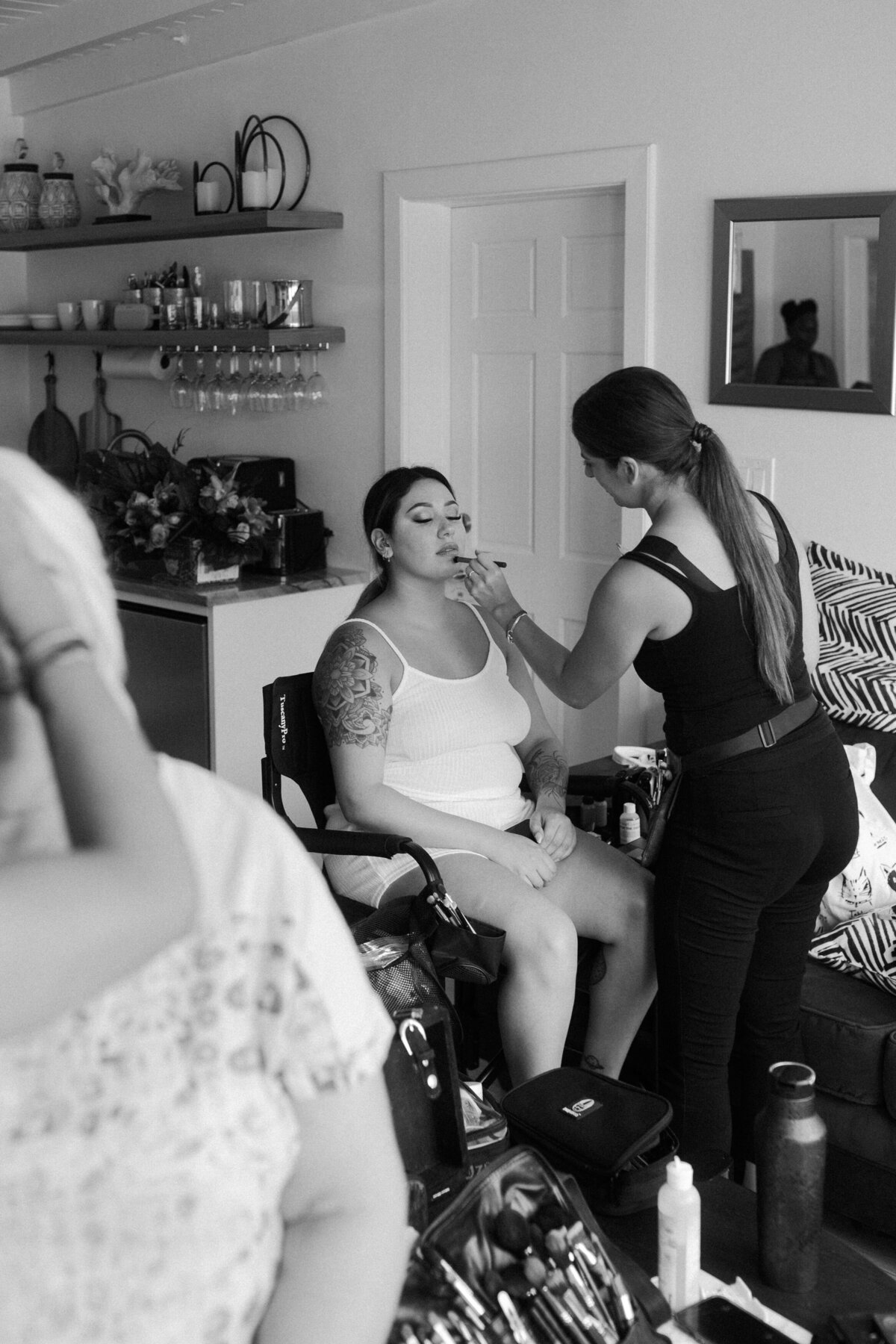 A black and white photo of a bride getting makeup done by a stylist
