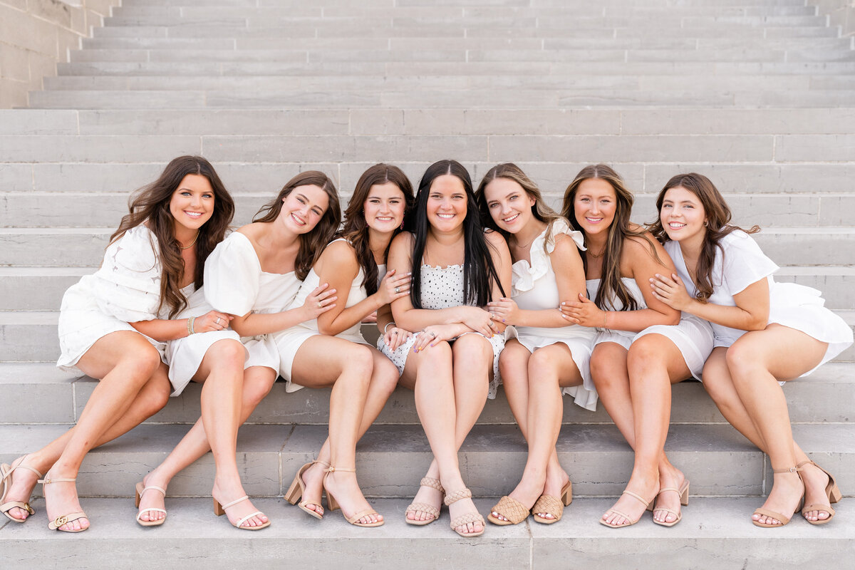 Texas A&M senior girls hugging each other while sitting on steps and smiling while wearing all white at the Administration Building