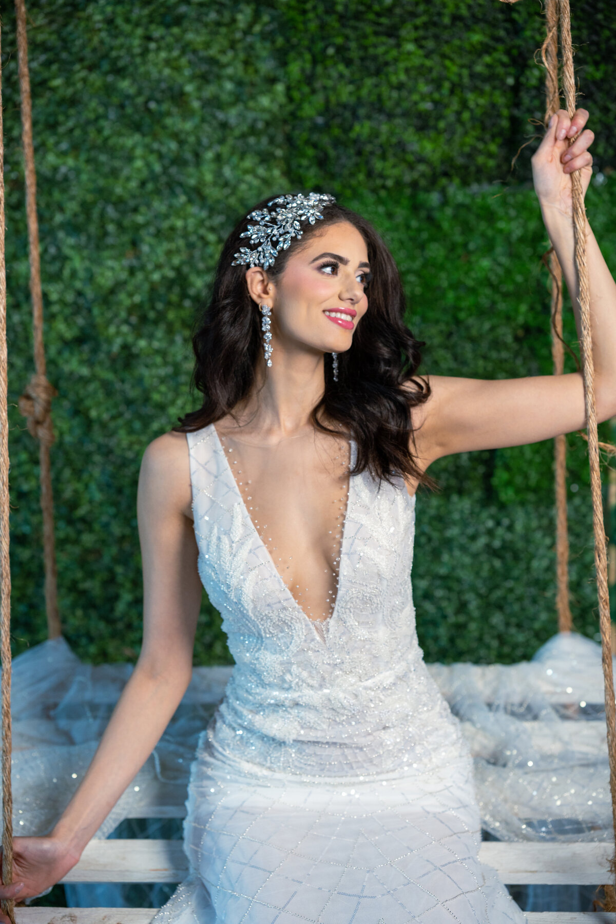 Stylish garden portrait of a bride wearing a V-neck beaded wedding dress sitting on a wood swing.